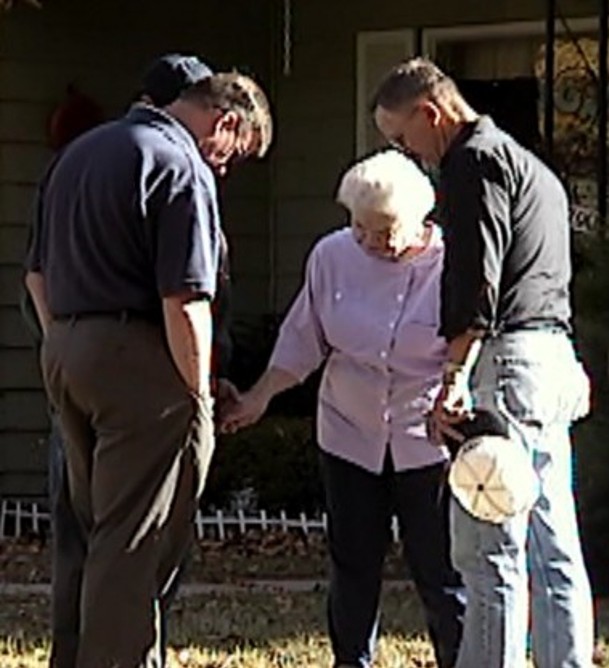 Team on front lawn praying with widow